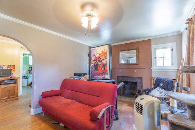 living area with arched walkways, light wood-style floors, and ornamental molding