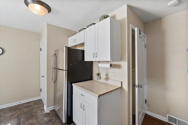 kitchen with visible vents, white cabinetry, freestanding refrigerator, and baseboards