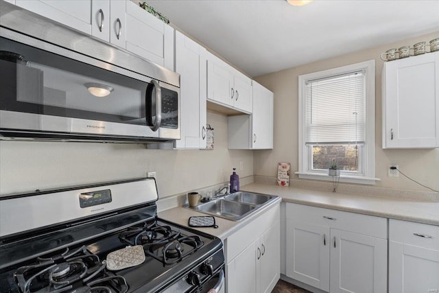 kitchen with a sink, stainless steel appliances, light countertops, and white cabinetry