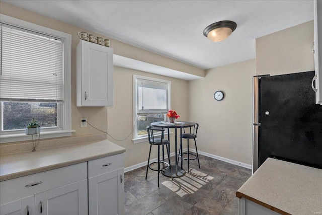 kitchen featuring baseboards, white cabinets, light countertops, and freestanding refrigerator