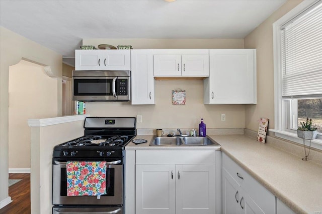 kitchen with a sink, wood finished floors, appliances with stainless steel finishes, white cabinets, and light countertops