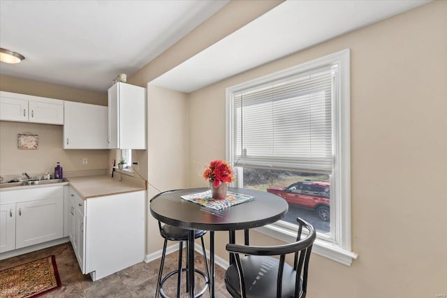 kitchen with a sink, baseboards, light countertops, and white cabinetry