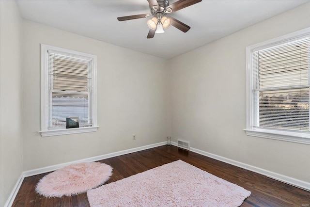 spare room featuring a ceiling fan, baseboards, visible vents, and dark wood-style flooring