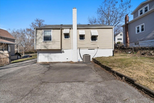 back of property featuring a chimney, central AC unit, and a lawn