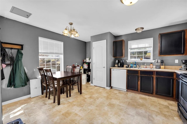 kitchen with baseboards, dishwasher, light countertops, a notable chandelier, and a sink