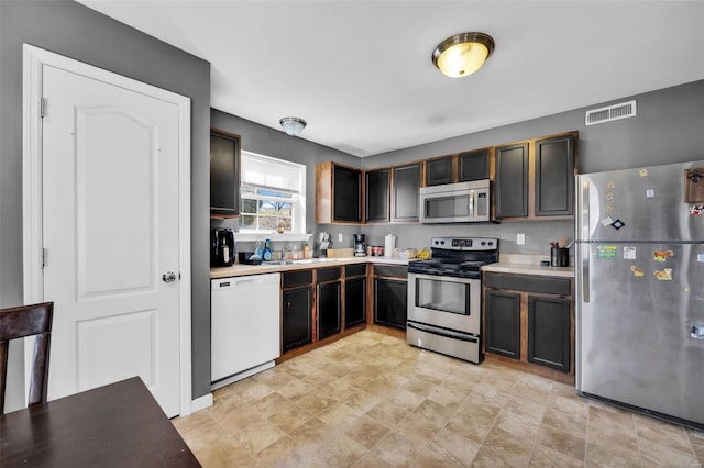 kitchen featuring visible vents, a sink, dark brown cabinetry, light countertops, and appliances with stainless steel finishes