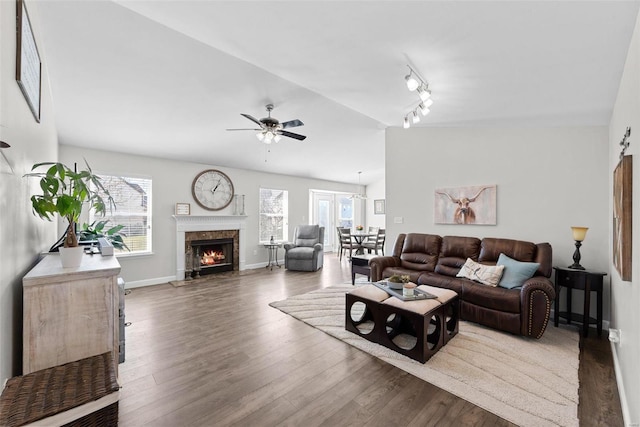 living room featuring a high end fireplace, baseboards, vaulted ceiling, wood finished floors, and a ceiling fan