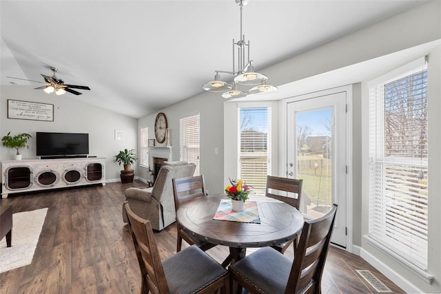 dining space with visible vents, vaulted ceiling, a fireplace, a ceiling fan, and dark wood-style flooring