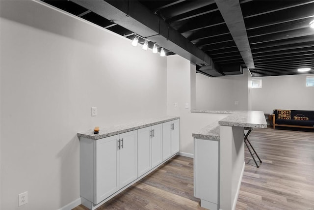 kitchen featuring white cabinetry, a kitchen breakfast bar, light wood-style floors, and baseboards