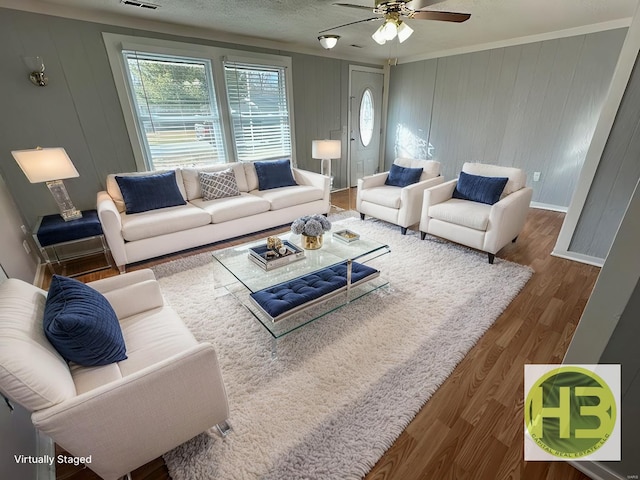 living area featuring visible vents, ornamental molding, a ceiling fan, wood finished floors, and baseboards