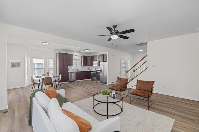 living area featuring stairway, baseboards, light wood-style floors, and ceiling fan