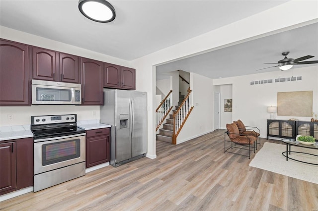 kitchen featuring open floor plan, stainless steel appliances, light wood-style floors, light countertops, and ceiling fan