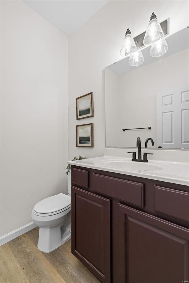 half bathroom featuring toilet, vanity, baseboards, and wood finished floors