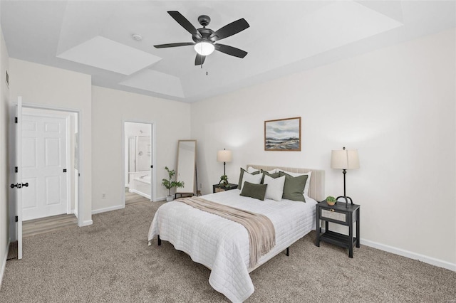 carpeted bedroom featuring ensuite bath, a tray ceiling, baseboards, and ceiling fan