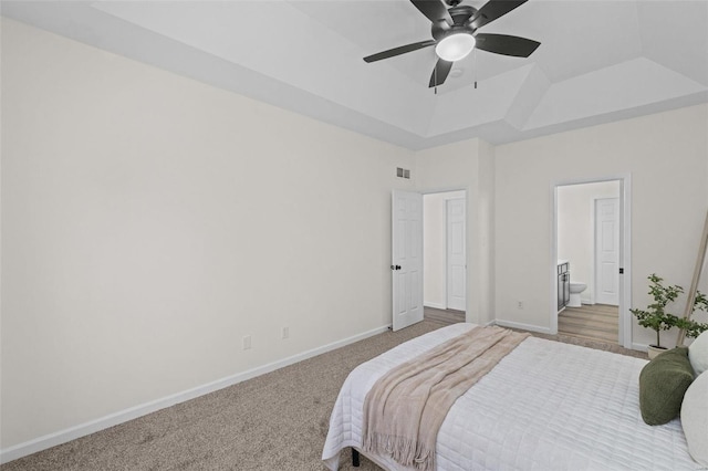 carpeted bedroom featuring visible vents, connected bathroom, baseboards, ceiling fan, and a tray ceiling