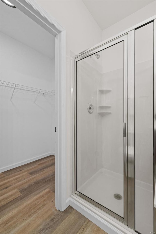 full bath with baseboards, wood finished floors, a stall shower, and a spacious closet