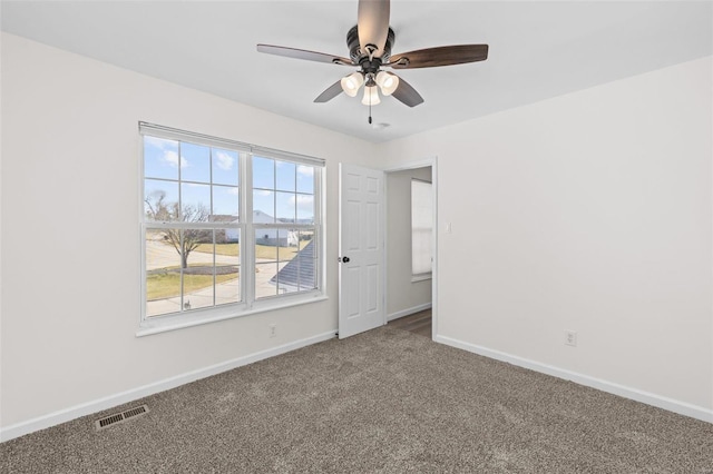 carpeted spare room with visible vents, baseboards, and a ceiling fan