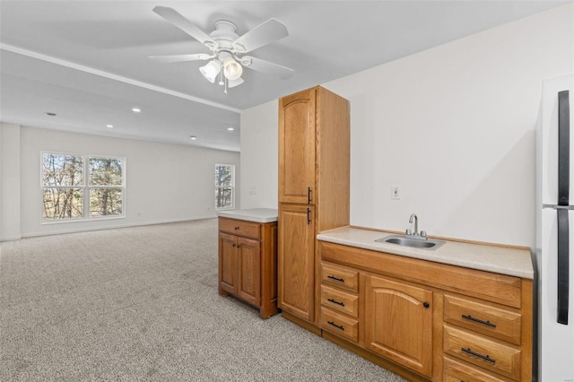 kitchen featuring freestanding refrigerator, a sink, light countertops, light colored carpet, and brown cabinets