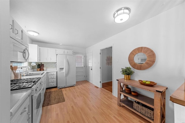 kitchen with tasteful backsplash, light countertops, light wood-style flooring, white appliances, and a sink