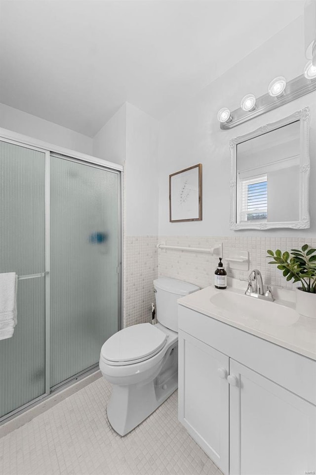 bathroom with vanity, a wainscoted wall, a stall shower, tile walls, and toilet