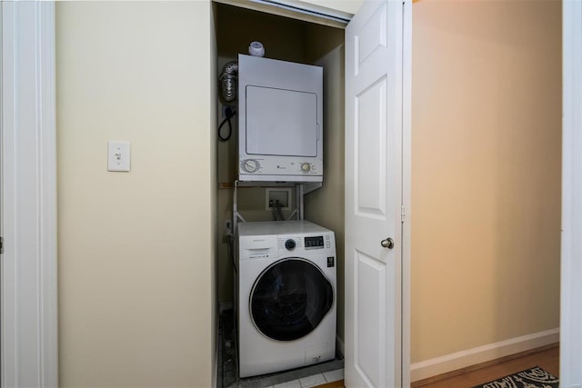 washroom with baseboards, laundry area, and stacked washing maching and dryer