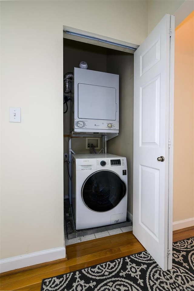 laundry area with laundry area, wood finished floors, baseboards, and stacked washer and dryer