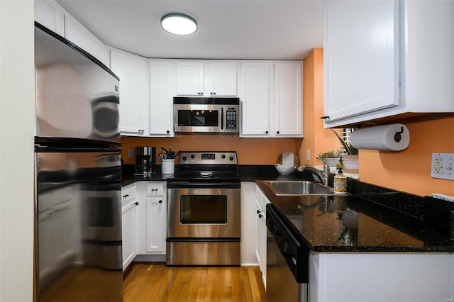 kitchen with a sink, dark stone countertops, stainless steel appliances, light wood-style floors, and white cabinets