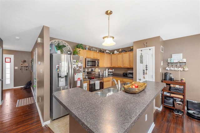 kitchen featuring dark countertops, light brown cabinets, appliances with stainless steel finishes, wood finished floors, and a sink