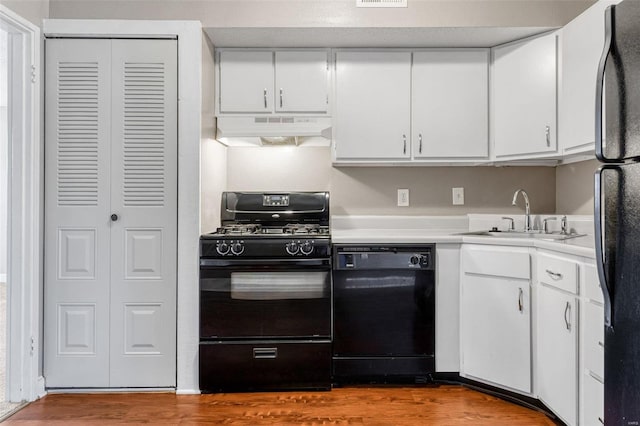 kitchen with wood finished floors, a sink, black appliances, under cabinet range hood, and white cabinetry