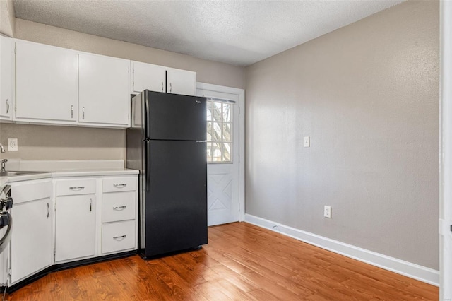 kitchen with wood finished floors, baseboards, freestanding refrigerator, a sink, and white cabinetry