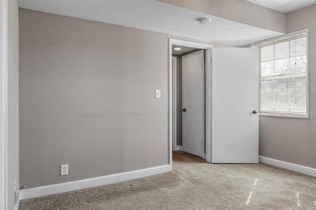 carpeted empty room featuring a textured wall, baseboards, and a textured ceiling