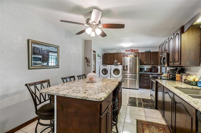 kitchen with light stone countertops, stainless steel appliances, a kitchen bar, independent washer and dryer, and a center island