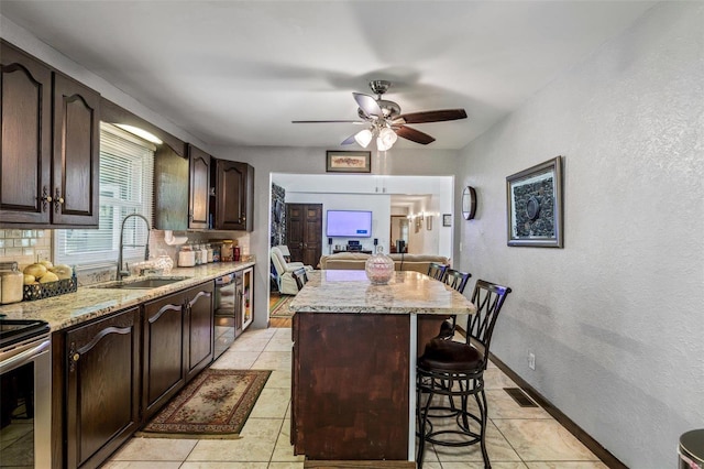 kitchen with light stone countertops, a breakfast bar, a sink, dark brown cabinetry, and a center island