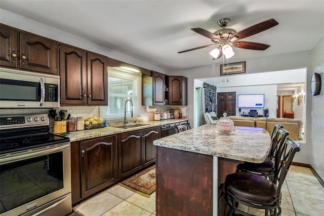 kitchen with light stone counters, a sink, stainless steel appliances, a kitchen breakfast bar, and a center island