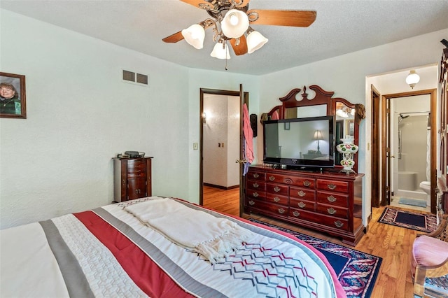 bedroom featuring visible vents, a textured ceiling, ensuite bath, wood finished floors, and ceiling fan