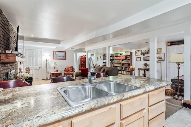 kitchen featuring a brick fireplace, light stone countertops, light brown cabinetry, open floor plan, and a sink