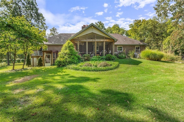 back of house with a yard, brick siding, a chimney, and a sunroom