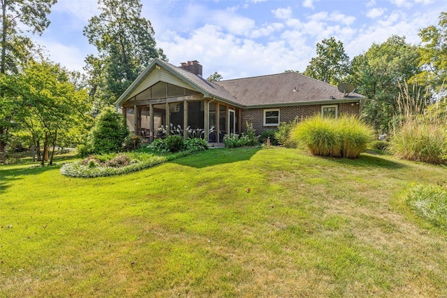 back of house with a yard, brick siding, a sunroom, and a chimney