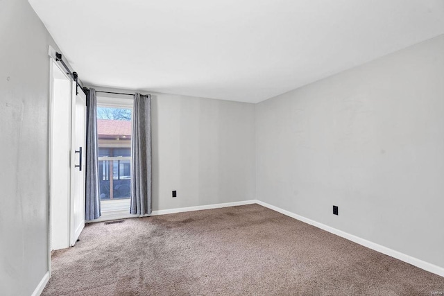 unfurnished room featuring baseboards, a barn door, carpet floors, and visible vents