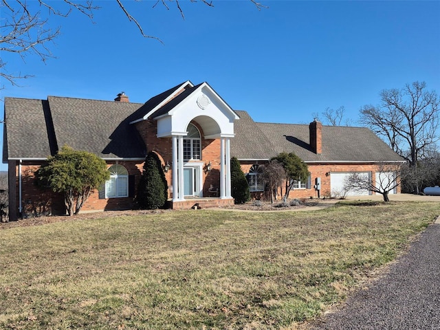 view of front of property with brick siding, a garage, a chimney, and a front yard