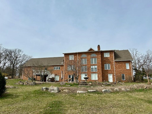 back of property featuring a lawn, brick siding, and a chimney