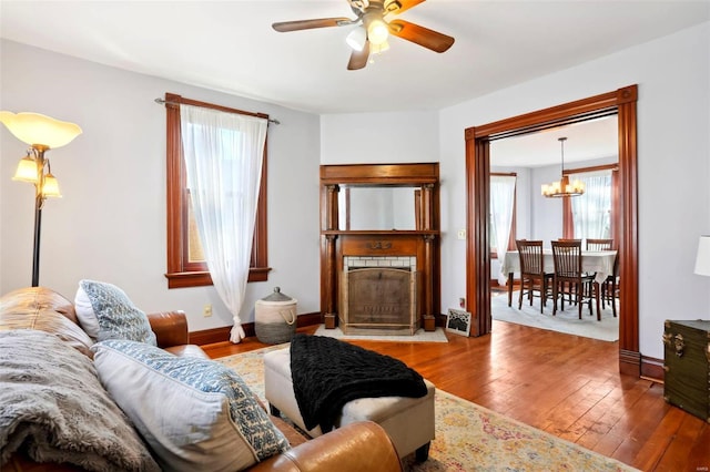 living area with ceiling fan with notable chandelier, a fireplace, baseboards, and hardwood / wood-style floors