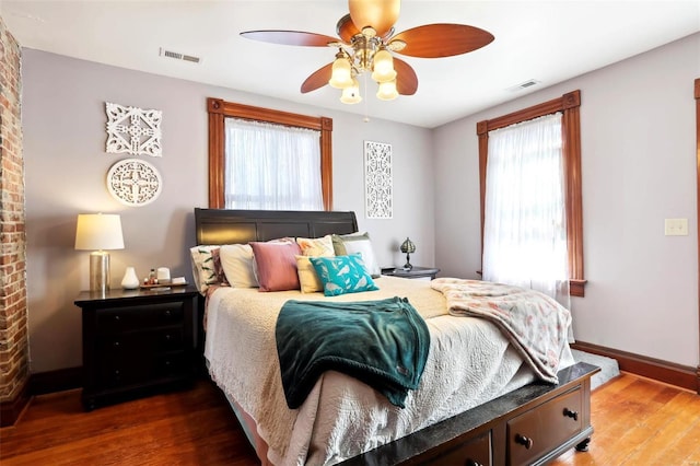 bedroom with ceiling fan, visible vents, baseboards, and wood finished floors