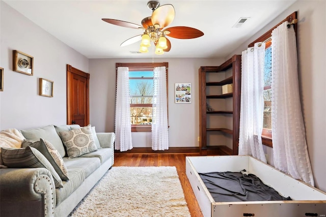 living area with visible vents, baseboards, ceiling fan, and wood finished floors