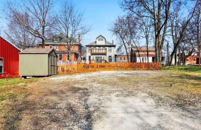 view of yard featuring an outdoor structure, a fenced front yard, a balcony, and a shed