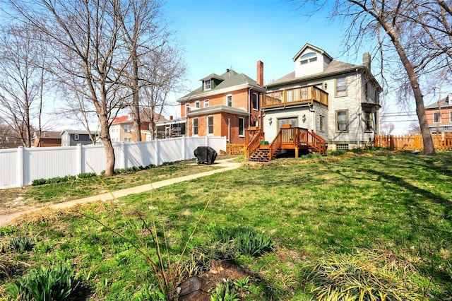 back of house featuring a balcony, a lawn, a fenced backyard, and a chimney