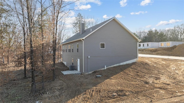 view of side of property with central AC unit, a chimney, and fence