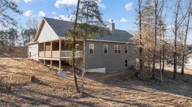 rear view of property featuring a chimney, ceiling fan, and a shingled roof