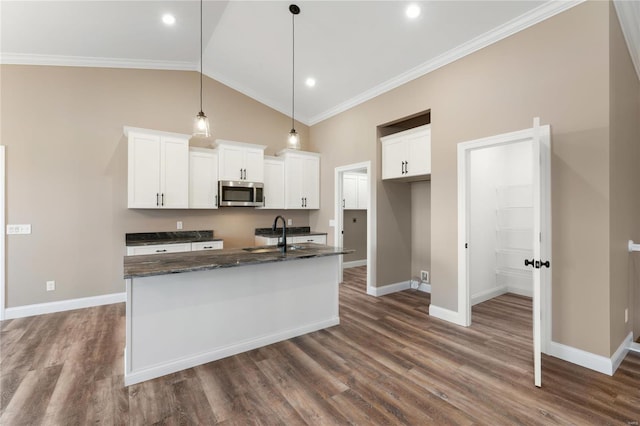 kitchen featuring a center island with sink, stainless steel microwave, baseboards, and ornamental molding