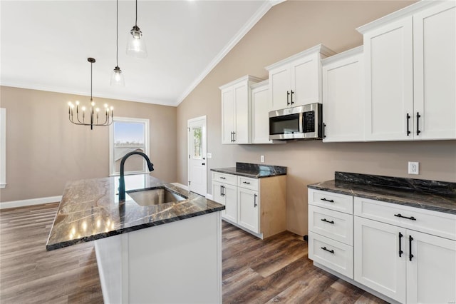 kitchen featuring dark stone countertops, a sink, vaulted ceiling, crown molding, and stainless steel microwave